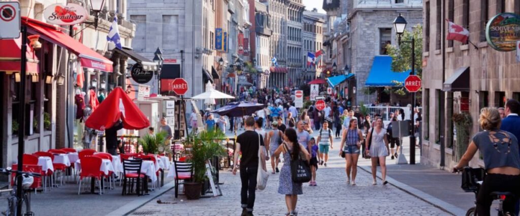 Crowded pedestrian street in Old Montreal lined with cafés, restaurants, and historic stone buildings on a sunny day.