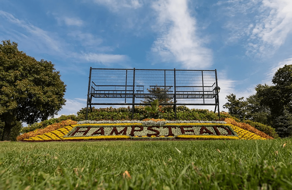 Hampstead welcome sign created with colorful flowers arranged in a landscaped garden under a blue sky.
