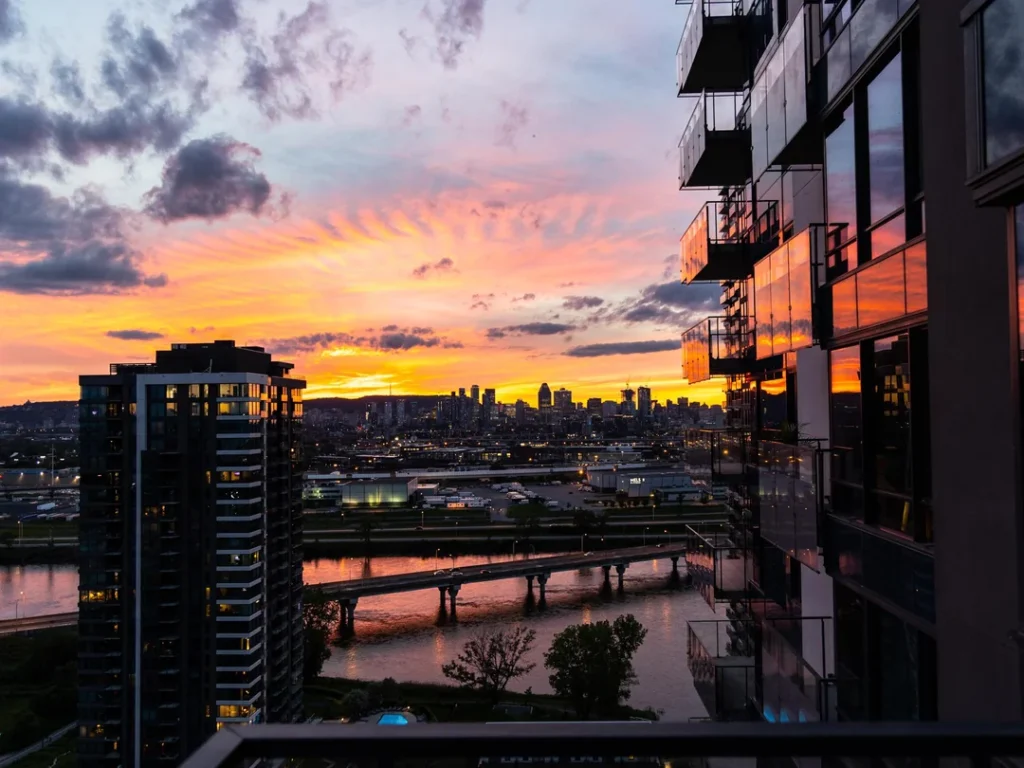 Sunset over Île des Sœurs, with high-rise buildings reflecting the orange sky and a river running between the cityscape.