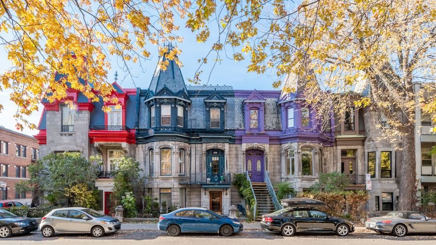 Row of colorful Victorian-style houses in Plateau-Mont-Royal, Montreal, with cars parked along a tree-lined street.